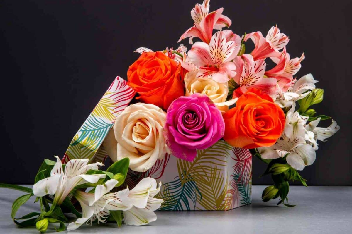 A side view bouquet colorful roses pink color alstroemeria flowers gift box placed on a black table.